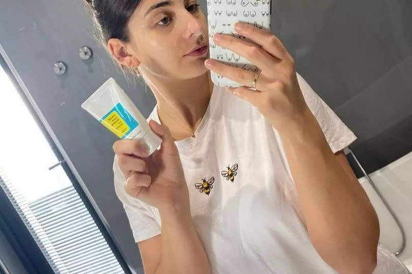 woman posing in mirror with soap on face holding product