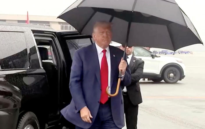 Donald Trump holding an umbrella against the rain as he leaves a black vehicle, wears a discontented expression. 