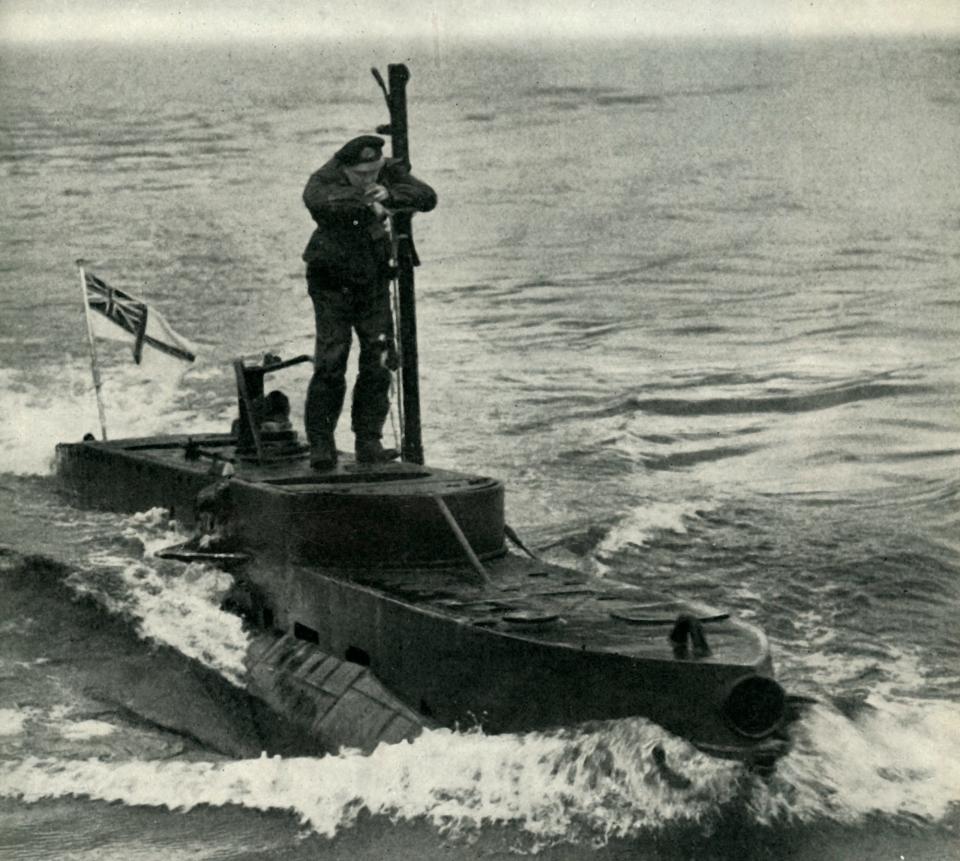 A person in an army uniform stands on a small submarine with a British flag on it