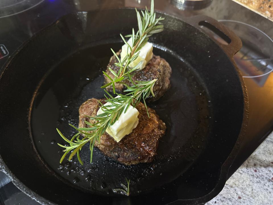 Two seared steaks in a cast iron skillet with large pads of butter and sprigs of rosemary on top of them