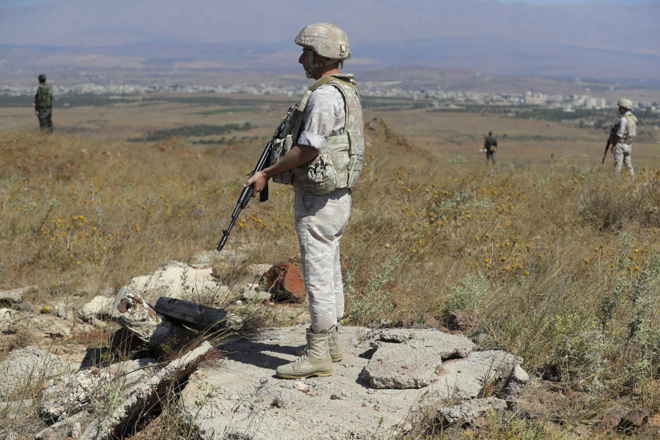 Russian military police officer, foreground, stand guard near the village of Tal Kroum, Syria, Tuesday, Aug. 14, 2018. The Russian military said Tuesday that its forces in Syria will help U.N. peacekeepers fully restore patrols along the frontier with the Israeli-occupied Golan Heights, reflecting Moscow's deepening role in mediating between the decades-old foes. (AP Photo/Sergei Grits)