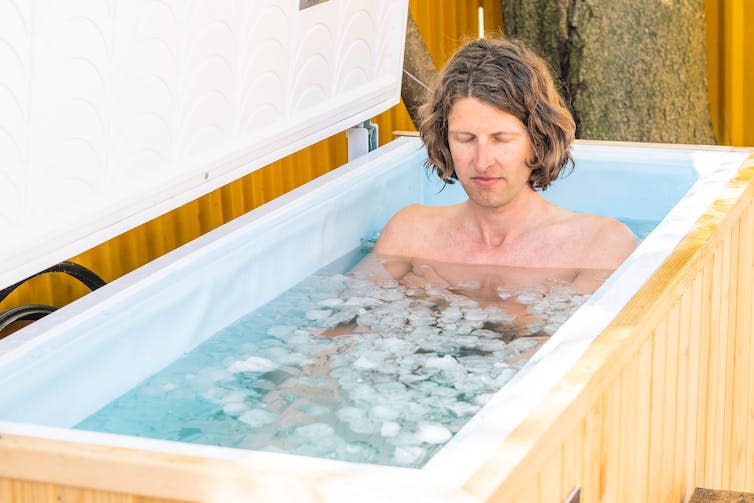 Boy or man with closed eyes bathing in the cold water among ice cubes