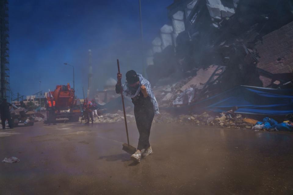 A Palestinian woman covers herself as truck sprays water in the street.