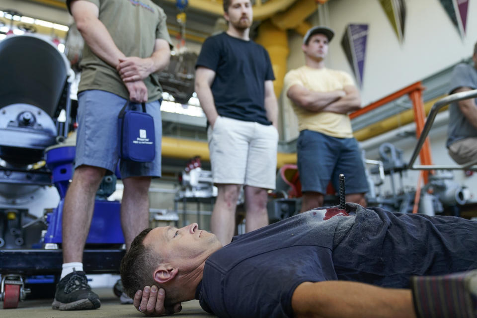 While Norm Witt, bottom, plays a victim of an accident, an instructor goes over the students' responses to the simulated incident during a Global Wind Organisation certification class at the Massachusetts Maritime Academy in Bourne, Mass., Thursday, Aug. 4, 2022. At the 131-year-old maritime academy along Buzzards Bay, people who will build the nation's first commercial-scale offshore wind farm are learning the skills to stay safe while working around turbines at sea. (AP Photo/Seth Wenig)