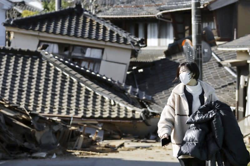 <cite>2024年1月2日，日本石川縣地震後，一名婦女走在倒塌的房屋前。（AP）</cite>