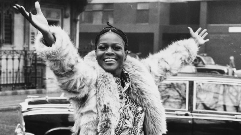 A young Cicely Tyson smiling and throwing her arms in the air while wearing a fur coat