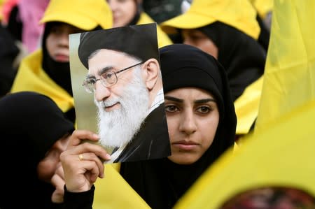 FILE PHOTO: A woman carries a picture of Iran's Supreme Leader Khamenei as she watches Lebanon's Hezbollah leader Nasrallah appear on a screen during a live broadcast to speak to his supporters at an event marking Resistance and Liberation Day in the Bekaa