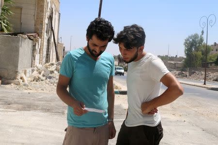 Men read one of the leaflets dropped by the Syrian army over opposition-held Aleppo districts asking residents to cooperate with the military and calling on fighters to surrender, Syria July 28, 2016. REUTERS/Abdalrhman Ismail