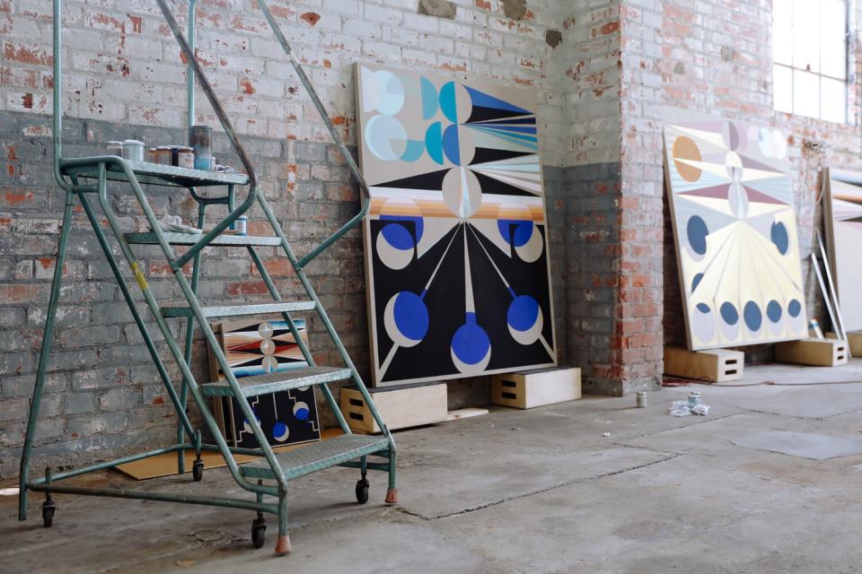 A step ladder and a series of in-progress paintings with circular patterns are seen inside a warehouse studio