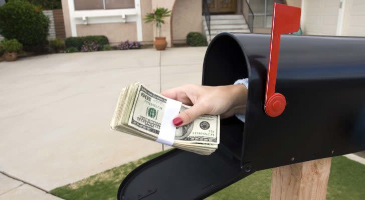 A hand reaches out of a mailbox holding a wad of cash.