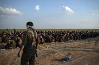 U.S.-backed Syrian Democratic Forces (SDF) fighters stand guard next to men waiting to be screened after being evacuated out of the last territory held by Islamic State militants, near Baghouz, eastern Syria, Friday, Feb. 22, 2019. (AP Photo/Felipe Dana)