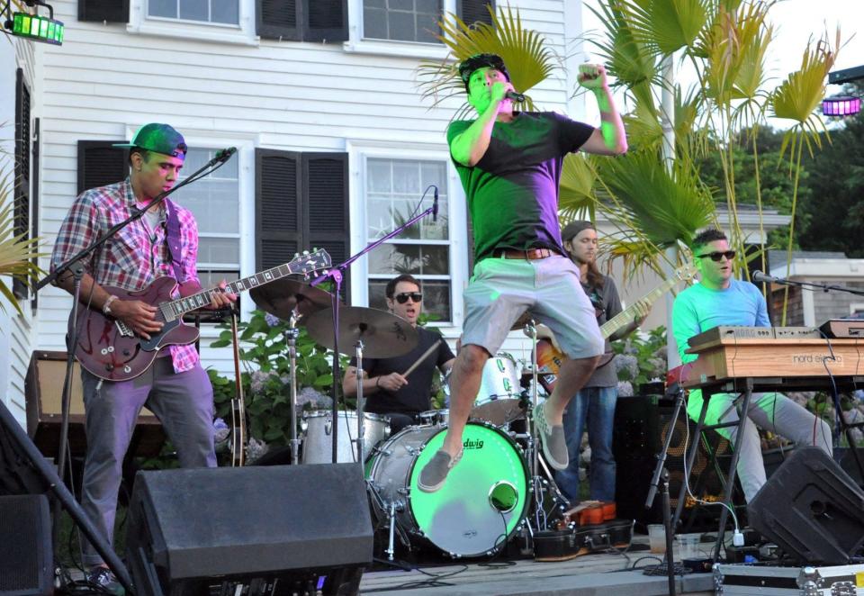 Aldous Collins Band lead singer Aldous Collins, of Hanover, center, leaps during a song at Roht Marine in Marshfield on July 28, 2021.
