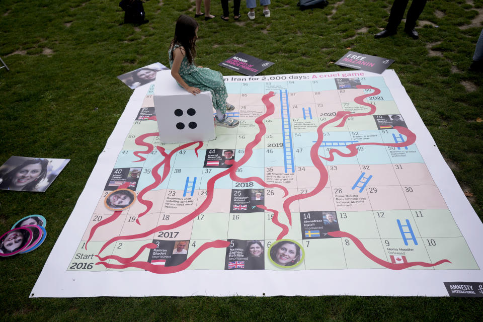 Gabriella, the seven year old daughter of imprisoned British-Iranian woman Nazanin Zaghari-Ratcliffe sits on a die on a giant snakes and ladders board in Parliament Square, London, to show the "ups and downs" of Zaghari-Ratcliffe's case to mark the 2,000 days she has been detained in Iran, Thursday, Sept. 23, 2021. Zaghari-Ratcliffe was originally sentenced to five years in prison after being convicted of plotting the overthrow of Iran's government, a charge that she, her supporters and rights groups deny. While employed at the Thomson Reuters Foundation, the charitable arm of the news agency, she was taken into custody at the Tehran airport in April 2016 as she was returning home to Britain after visiting family. (AP Photo/Matt Dunham)