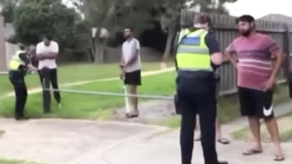 A group of Victorians stand around and appear to cop fines after playing backyard cricket.