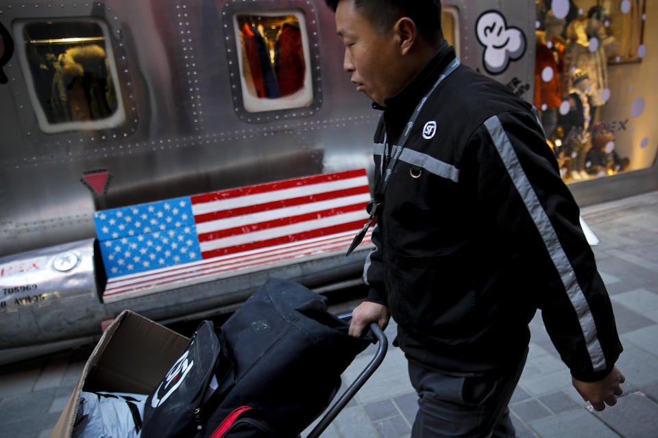 A delivery worker pushes a cart loaded with goods past by a bench with an American flag outside a fashion boutique selling U.S. brand clothing at the capital city's popular shopping mall in Beijing, Friday, Feb. 1, 2019. U.S. President Donald Trump expects to meet with his Chinese counterpart Xi Jinping to try to resolve a six-month trade standoff after U.S. and Chinese negotiators ended two days of talks Thursday without settling the toughest issues that divide the world's two biggest economies. The White House says the two countries made progress but "much work remains to be done." (AP Photo/Andy Wong)