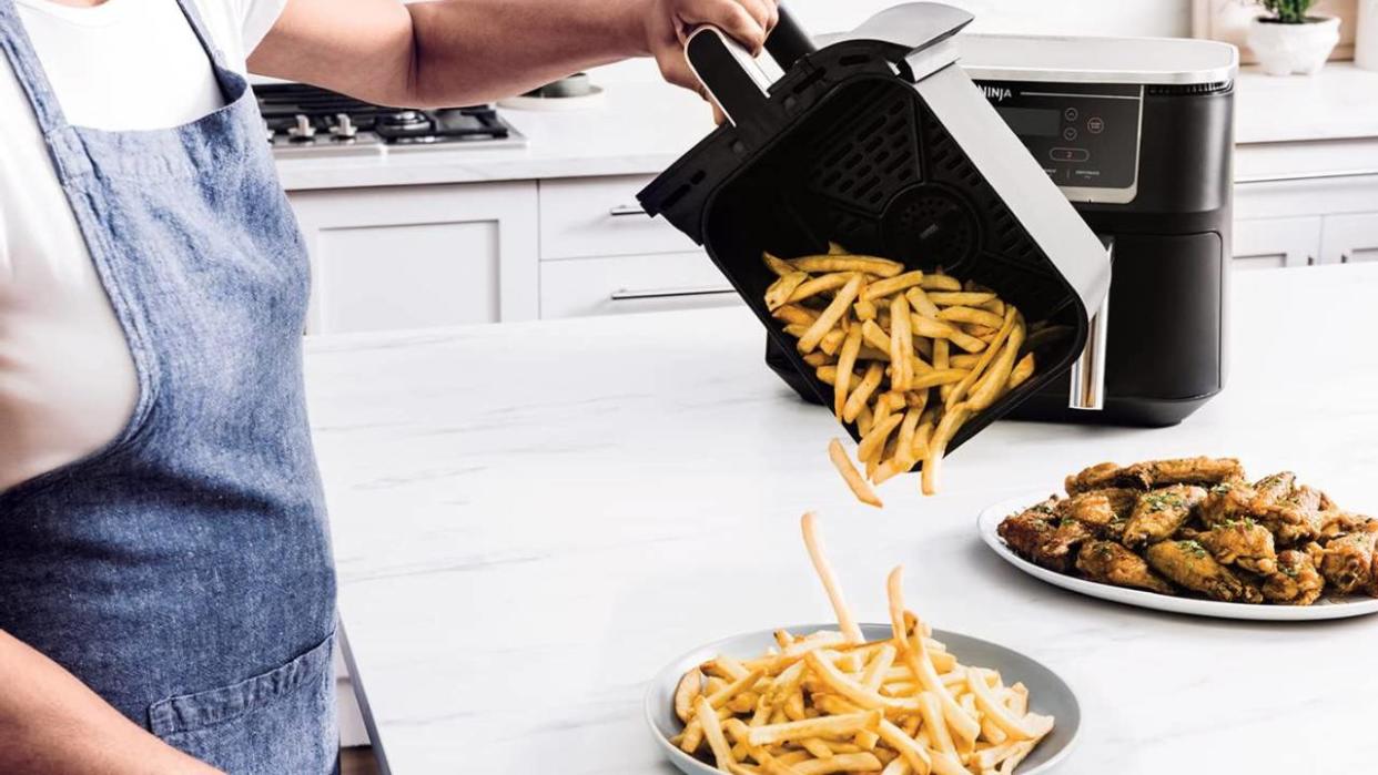  Someone tipping chips out of an air fryer basket onto a plate. 