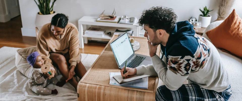 Man working from home on laptop, woman and baby playing on floor