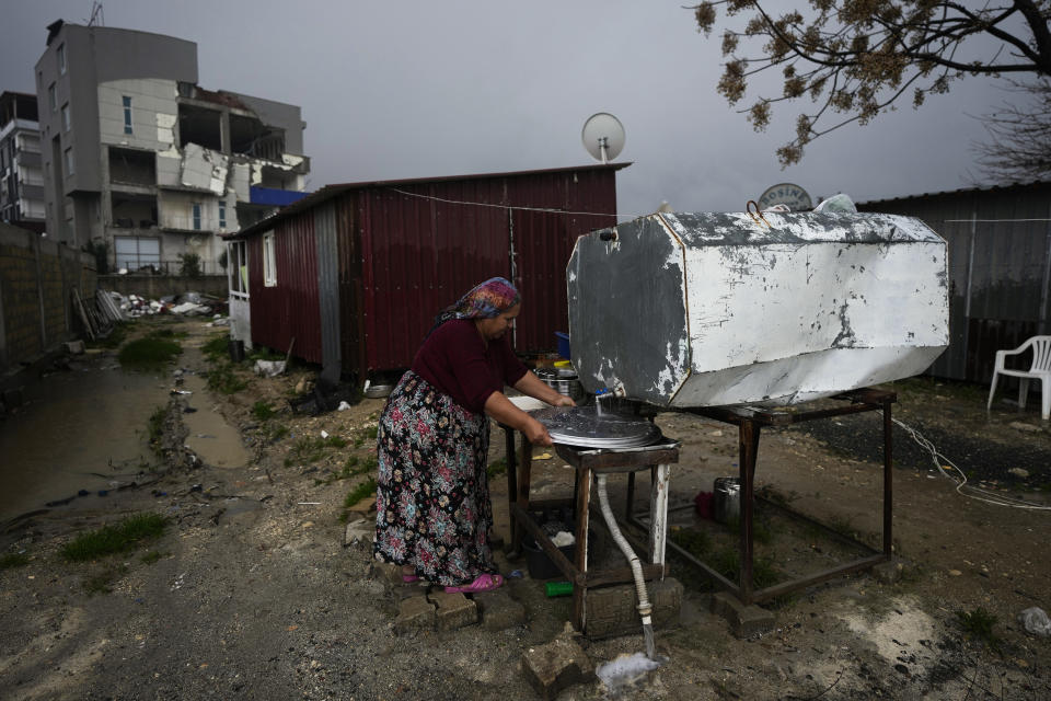 An elderly woman washes dishes outside a container house she and her family shelter in after the powerful Feb. 6, 2023 earthquake hit in Antakya, southern Turkey, Friday, Jan. 12, 2024. Many in the region are still struggling to rebuild lives a year after the devastation. (AP Photo/Khalil Hamra)