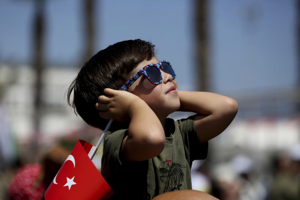 A boy holding a Turkish flag watches as Turkish acrobatic jets fly, during a military parade celebration marking the 45th anniversary of the 1974 Turkish invasion in the Turkish occupied area of the divided capital Nicosia, Cyprus, Saturday, July 20, 2019. Cyprus was split into Greek Cypriot south and Turkish Cypriot north in 1974 when Turkey invaded in response to a coup by supporters of a union with Greece. (AP Photo/Petros Karadjias)