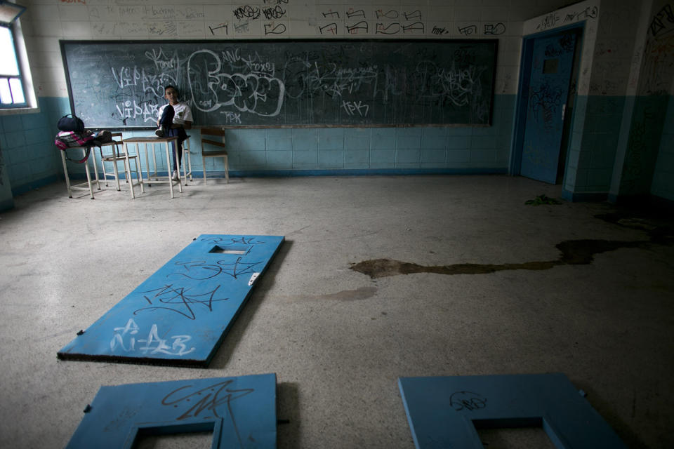 <p>A student sits on a teacher’s desk inside what was once a classroom, where doors lay on the floor as well as urine, at a public high school in Caracas, Venezuela, June 1, 2016. The social and economic chaos stalking Venezuela is ripping apart its once-enviable school system, robbing poor students of what would otherwise be their best chance to escape lives fast becoming unbearable. (Ariana Cubillos/AP) </p>