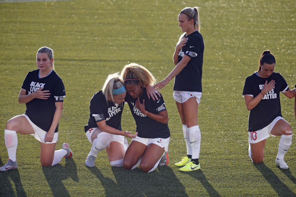 Chicago Red Stars' Julie Ertz, second from left, holds Casey Short, center, while other players for the team kneel during the national anthem before an NWSL Challenge Cup soccer match against the Washington Spirit at Zions Bank Stadium, Saturday, June 27, 2020, in Herriman, Utah. (AP Photo/Rick Bowmer)