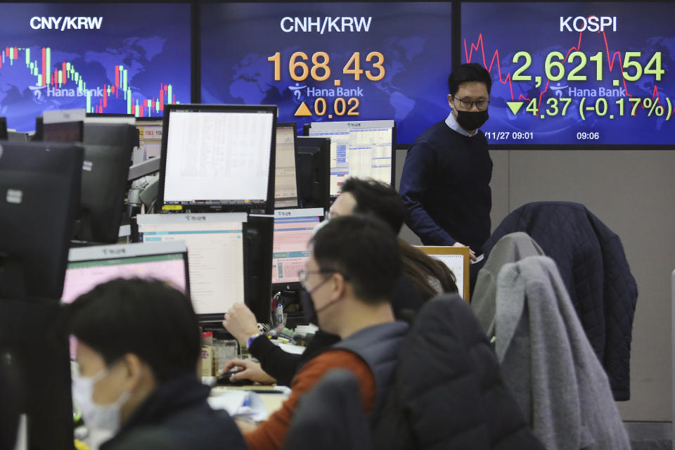 A currency trader passes by screens showing the Korea Composite Stock Price Index, right, and the foreign exchange rate at the foreign exchange dealing room of the KEB Hana Bank headquarters in Seoul, South Korea, Friday, Nov. 27, 2020. Asian stock markets declined Friday as questions about the effectiveness of one possible coronavirus vaccine weighed on investor optimism. (AP Photo/Ahn Young-joon)