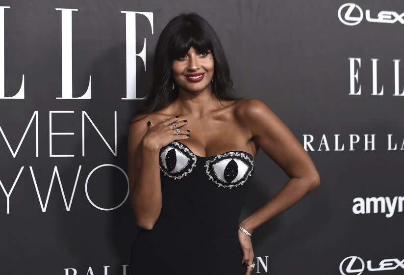 A woman with long dark hair and bangs poses in a black dress