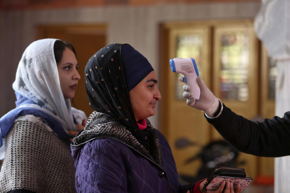 A volunteer, checks the temperature of a woman as Sikh devotees, arrive to offer prayers during celebrations to mark the birth anniversary of the first Sikh Guru, Guru Nanak Dev, at a Gurudwara, or Sikh temple, in Jammu, India, Monday, Nov.30, 2020. India is second behind the U.S. in total coronavirus cases. Its recovery rate is nearing 94%. (AP Photo/Channi Anand)