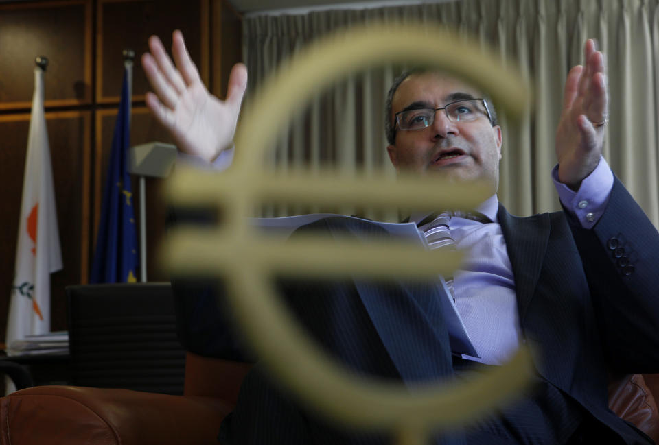 FILE - In this Tuesday, Jan. 15, 2013 file photo, seen through a euro sign, Cyprus’ Central Bank chief Panicos Demetriades gestures during an interview with The Associated Press at his office in central bank of Cyprus in capital Nicosia, Cyprus. Demetriades has resigned just as the bailed-out country struggles to emerge from a deep recession, according to a government statement Monday, March 10, 2014. (AP Photo/Petros Karadjias, File)