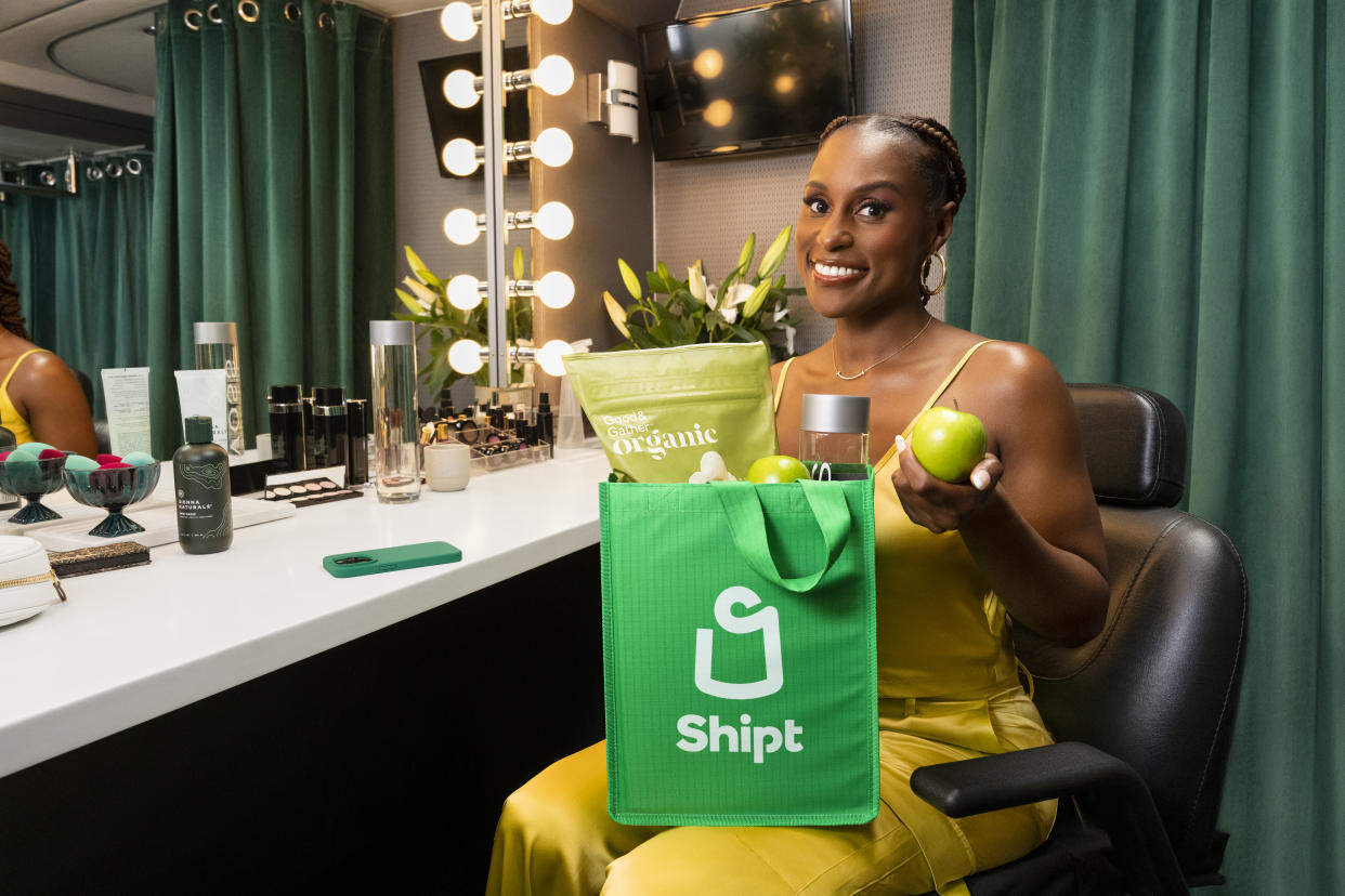 Issa Rae on set sitting in a chair with a shipt bag in her lap