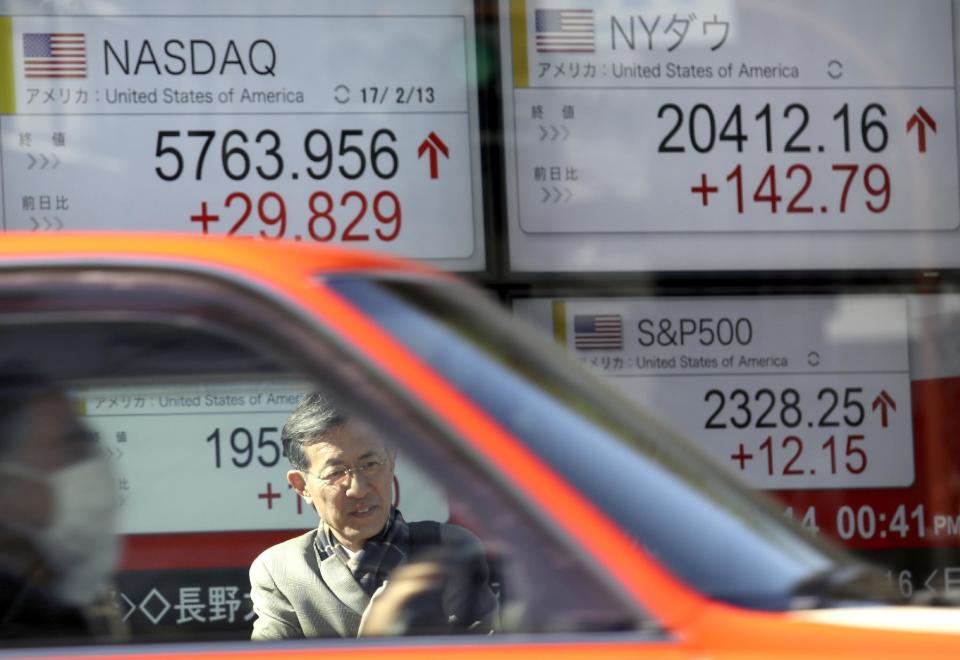 A man waits to cross a street in front of an electronic stock indicator of a securities firm in Tokyo, Tuesday, Feb. 14, 2017. Shares in Asia fell back after an early rally on Tuesday, as investors awaited comments to Congress by Federal Reserve chair Janet Yellen. (AP Photo/Shizuo Kambayashi)