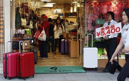 Tourists look at items inside a store as a man holds a banner reading, "All items 5,400 Japanese Yen", along a street at Tokyo's Ginza Shopping district May 16, 2014. REUTERS/Yuya Shino