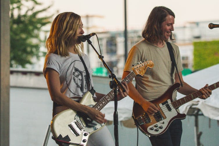 Woman Playing Guitar While Singing Beside Man Playing Bass Guitar Near Microphone.