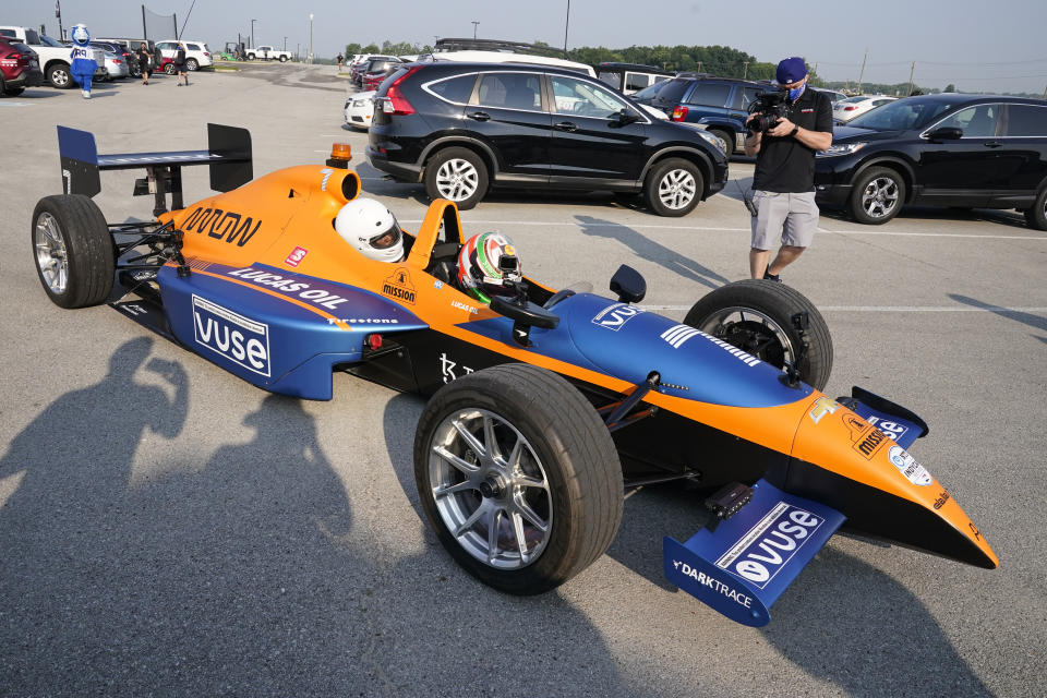 Indianapolis Colts corner back Kenny Moore II arrives in the back seat of a two-seat IndyCar driven by IndyCar driver Pato O'Ward as the players reported to the NFL team's football training camp in Westfield, Ind., Tuesday, July 27, 2021. Practice open on Wednesday. (AP Photo/Michael Conroy)