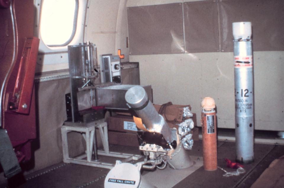 inside an aircraft cabin, a small metal cylinder rests on top of a slide that goes through the floor