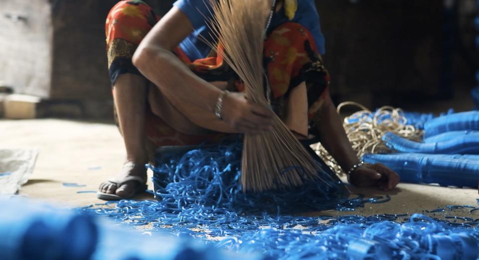 A women sweeps bright blue broken bangles from the floor