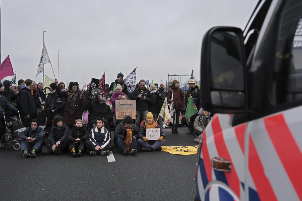 Climate activists sit on the ground, in front of a police van, blocking the main highway around Amsterdam near the former headquarters of a ING bank to protest its financing of fossil fuels, Saturday, Dec. 30, 2023. Protestors walked onto the road at midday, snarling traffic around the Dutch capital in the latest road blockade organized by the Dutch branch of Extinction Rebellion. (AP Photo/Patrick Post)