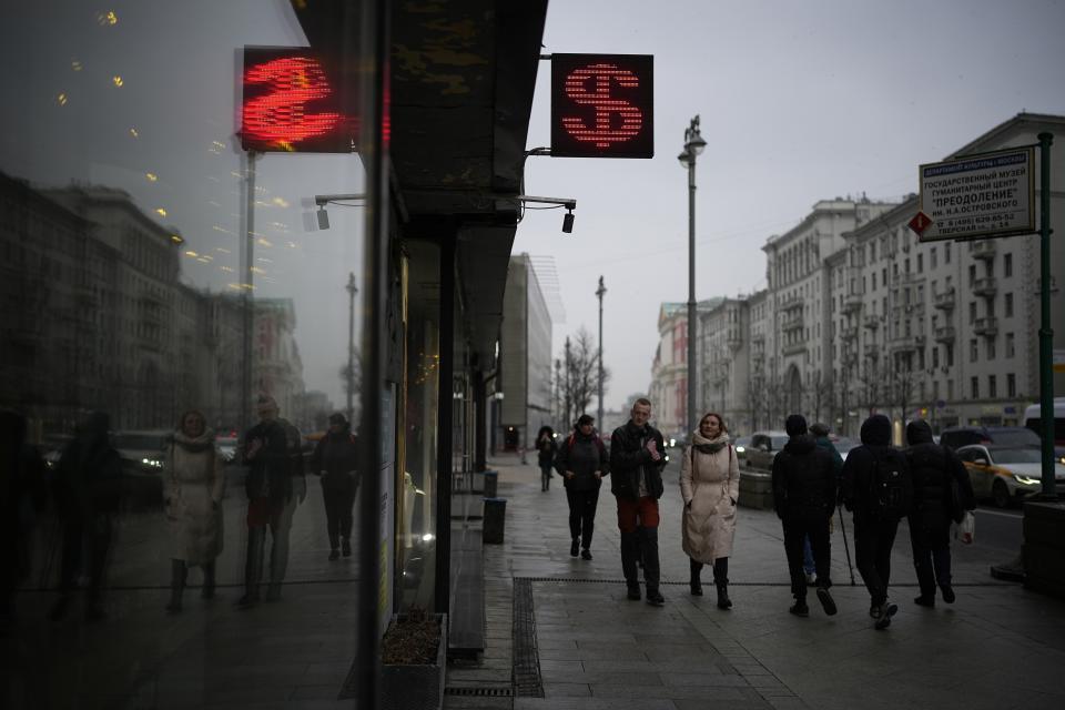FILE - People walk past a currency exchange office screen displaying the exchange rates of U.S. Dollar and Euro to Russian Rubles in Moscow's downtown, Russia, on March 29, 2022. Driven by moral outrage over Russia’s invasion of Ukraine, U.S. governors and other top state officials made it clear: They wanted to cut any financial ties with Russia. (AP Photo, File)