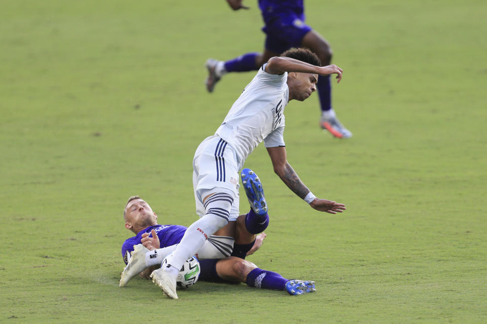 Orlando City defender Robin Jansson, bottom, slide-tackles New England Revolution forward Tajon Buchanan (17) during the second half of an MLS playoff soccer match, Sunday, Nov. 29, 2020, in Orlando, Fla. (AP Photo/Matt Stamey)