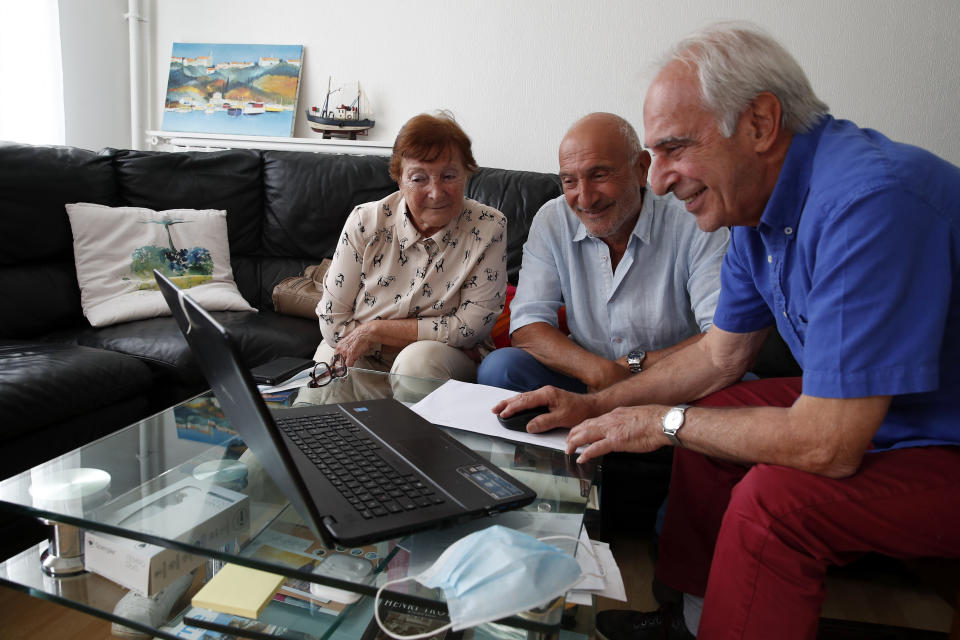 In this photo taken on June 5, 2020, Monette Hayoun, Dr Robert Haiun, and Gilbert Haiun, from left, look at photos of their brother Meyer Haiun on a computer during an interview in Ivry sur Seine, south of Paris. Families whose elders died behind the closed doors of homes in lockdown are filing wrongful death lawsuits, triggering police investigations. One suit focuses on the death of Meyer Haiun, a severely disabled 85-year-old in a Paris home managed by a Jewish charitable foundation headed Eric de Rothschild, scion of Europe's most famous banking dynasty. (AP Photo/Francois Mori)