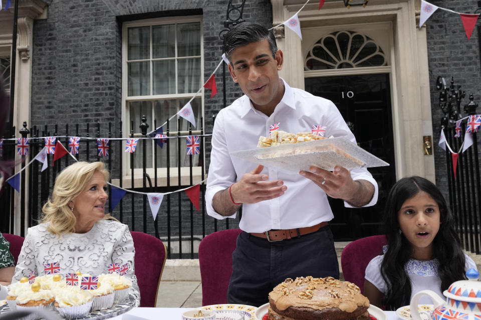 Prime Minister Rishi Sunak holds a plate of sandwiches as US First Lady Jill Biden looks on as they attend the Big Lunch party at Downing Street in London Sunday, May 7, 2023. The Big Lunch is part of the weekend of celebrations for the Coronation of King Charles III. Guests at the big lunch include community heroes and Ukrainians displaced by the war, and youth groups. (AP Photo/Frank Augstein, Pool)