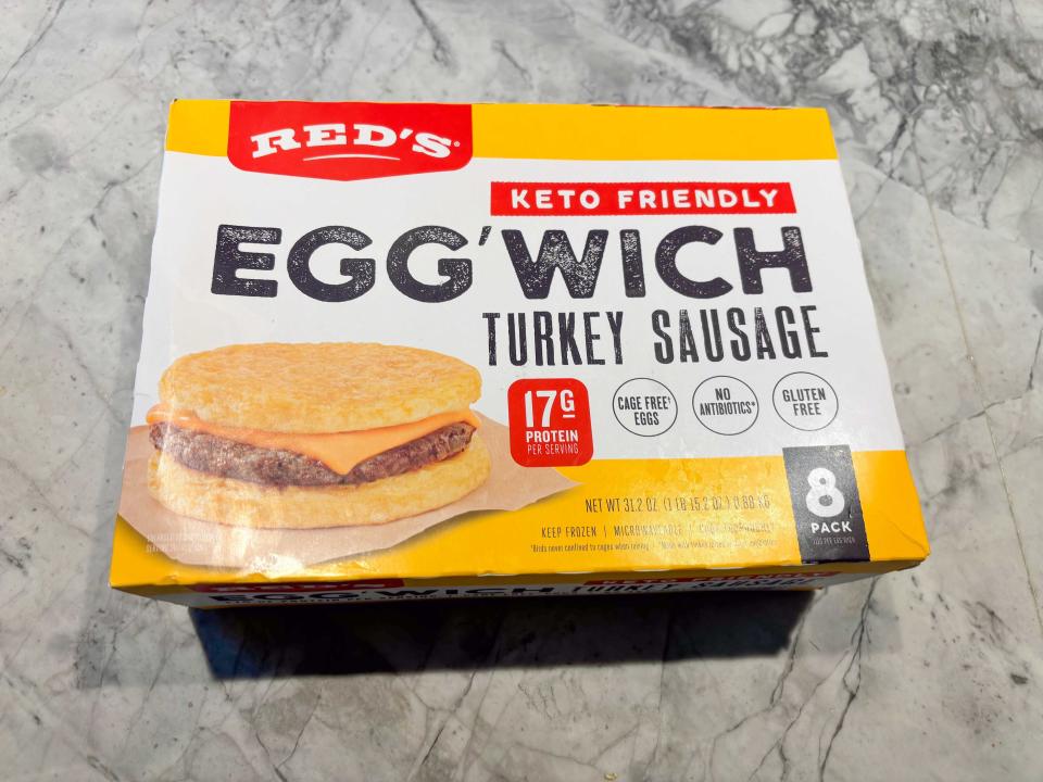A yellow and white box with red Red's logo and an image of an egg'wich, with two egg patties, a sausage, and a cheese slice on it