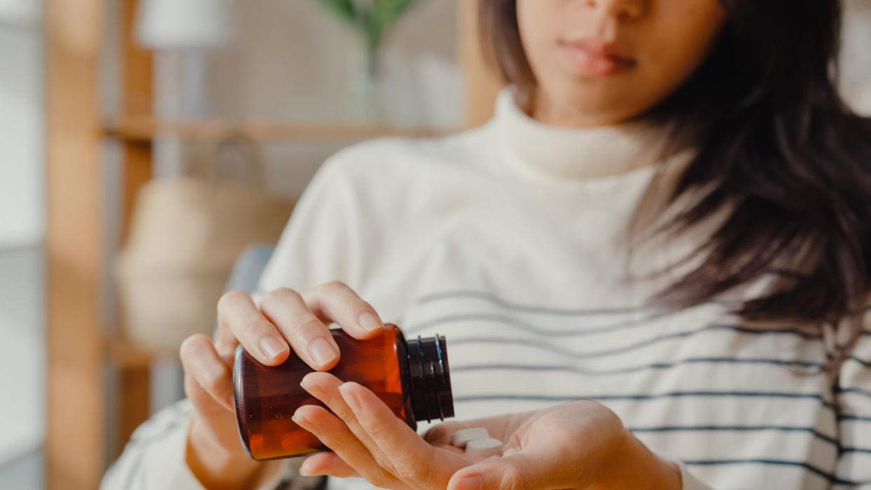 Sick young Asia woman holding pill take a look medicine sit on couch at home. Girl taking medicine after doctor order, quarantine at house, Coronavirus social distancing quarantine concept.