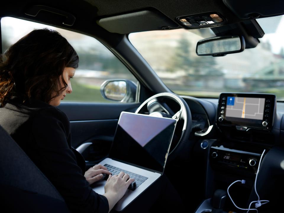 Businesswoman working on laptop in driverless car.