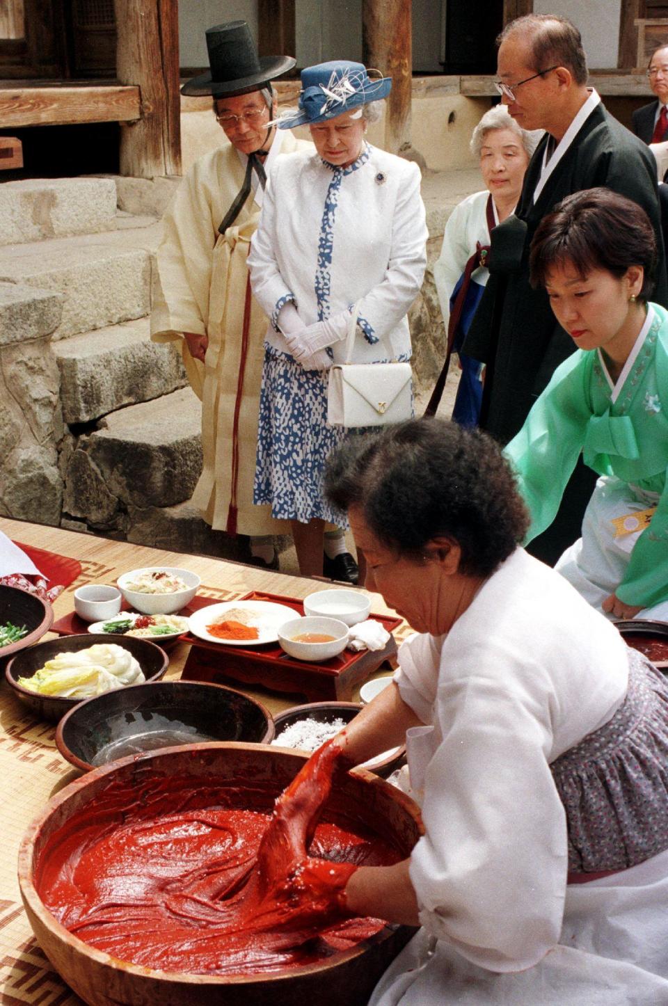 Britain's Queen Elizabeth II (C, top) watches women make South Korean's main side dish Kimchi as she visits a 400-year-old traditional house in the village of Hahoe, Andong province, 268 kilometers southeast of Seoul, 21 April 1999. South Korean aristocrat Ryu Yong-Ha, (R, top) the village chief, who is resisting changes to the country's millenia-old culture, didn not allow the Queen into his main living room which is strictly reserved for men. He disapproved of his relatives' plan to break with tradition and offer the monarch a birthday feast which he views as a demeaning publicity stunt.  AFP PHOTO/CHOO YOUN-KONG (Photo credit should read CHOO YOUN-KONG/AFP via Getty Images)