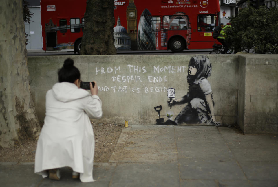 A woman takes a picture of a new piece of street art that people noticed for the first time last night and is believed to be by street artist Banksy on a wall where Extinction Rebellion climate protesters had set up a camp in Marble Arch, London, Friday, April 26, 2019. Extinction Rebellion ended its remaining blockades in London on Thursday evening with a closing ceremony, after disrupting the British capital for 10 days. The non-violent protest group is seeking negotiations with the government on its demand to make slowing climate change a top priority. (AP Photo/Matt Dunham)