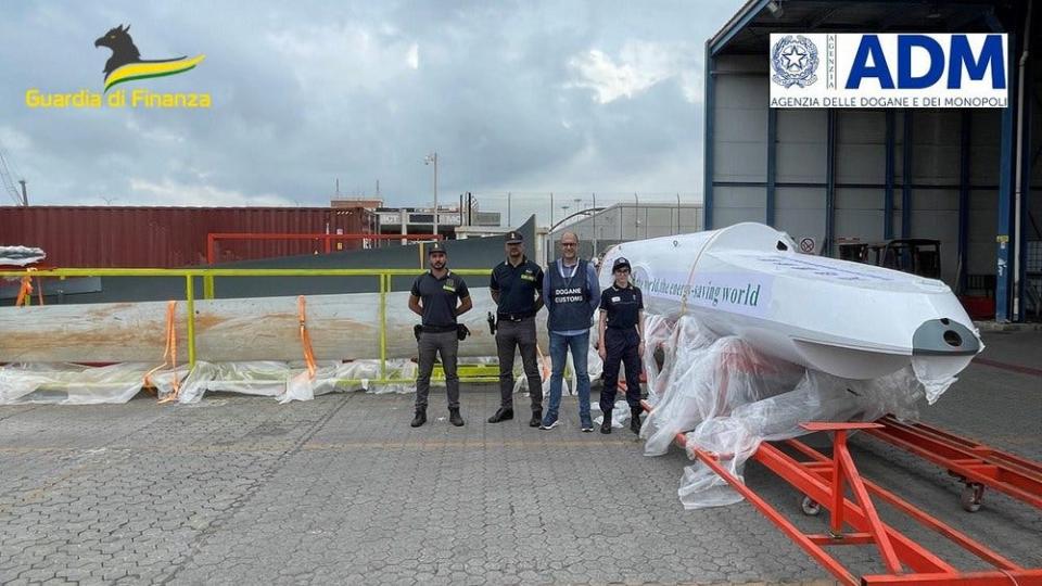 Italian officials stand next to drone parts disguised as wind turbines.