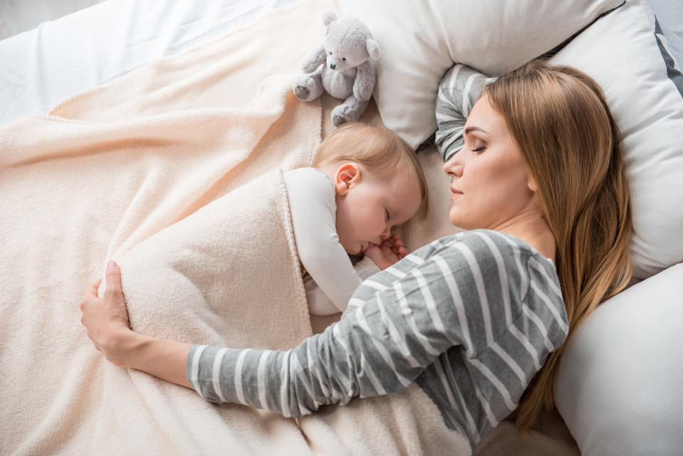 Top view of peaceful mother and cute child lying on double bed. They are sleeping together with tranquility