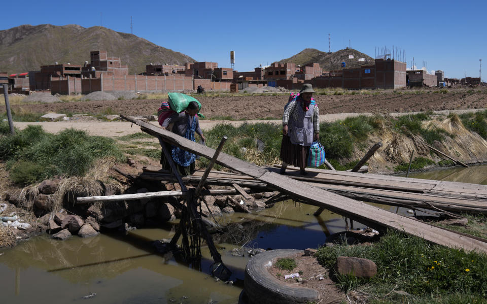 Women walk past roadblocks set up by anti-government protesters, to cross the border to Bolivia, in Desaguadero, Peru, Friday, Jan. 13, 2023. (AP Photo/Juan Karita)