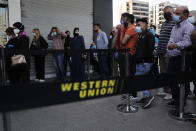 Lebanese citizens wear masks and gloves to help curb the spread of the coronavirus, as they queuing outside a Western Union shop to receive their money transfer in U.S. dollar currency, during the last day that they are allowed to dispense dollars to customers following new Central Bank rules, in Beirut, Lebanon, Thursday, April 23, 2020. Lebanon's currency continued its downward spiral before the dollar on Thursday, reaching a new low amid financial turmoil in the crisis-hit country. (AP Photo/Hussein Malla)